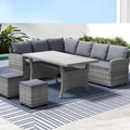 Grey wicker outdoor sectional sofa with dining table and ottomans on striped rug by poolside